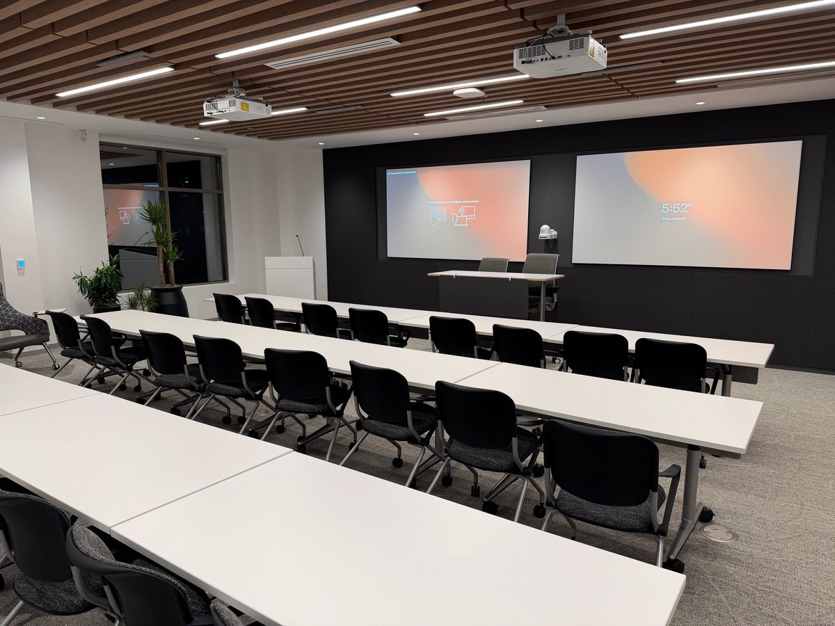 Training classroom with dual projection screens, ceiling projectors, and rows of tables, by Enlightened Audiovisual