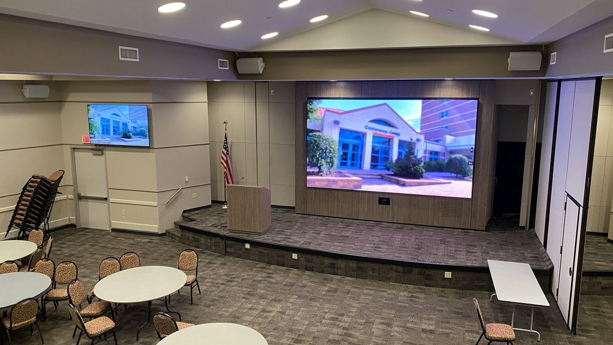 Conference center with a large LED stage display, side displays, and a presentation lectern, installed by Enlightened Audiovisual
